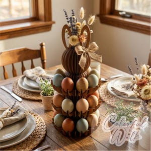 Puede incluir: Un soporte de madera para huevos de Pascua con dise&ntilde;o de orejas de conejo, lleno de huevos coloridos. El soporte est&aacute; decorado con flores secas y un lazo de arpillera. Los huevos son en tonos azules, naranjas y crema. Incluye manteles individuales tejidos.