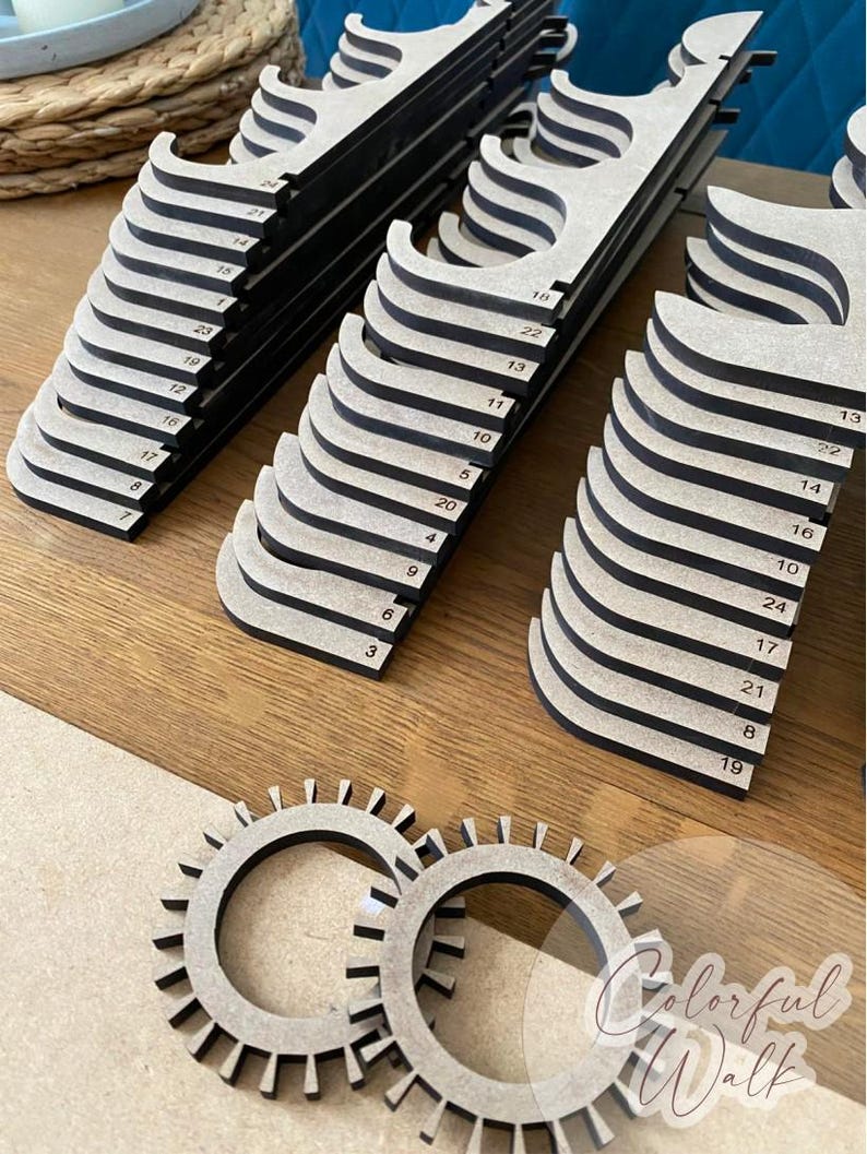 Puede incluir: Una colecci&oacute;n de expositores de madera con un dise&ntilde;o en capas, de color madera natural con bordes negros. Cada soporte est&aacute; numerado. Tambi&eacute;n hay dos piezas circulares de madera con forma de engranaje.