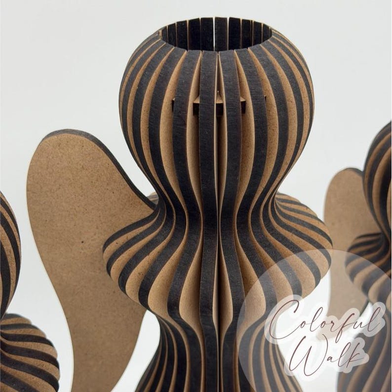 May include: A decorative angel figurine constructed from layered, vertical slats of dark brown and light tan wood. The structure features a rounded head and torso with prominent wings extending from the sides. The text Colorful Walk is visible.