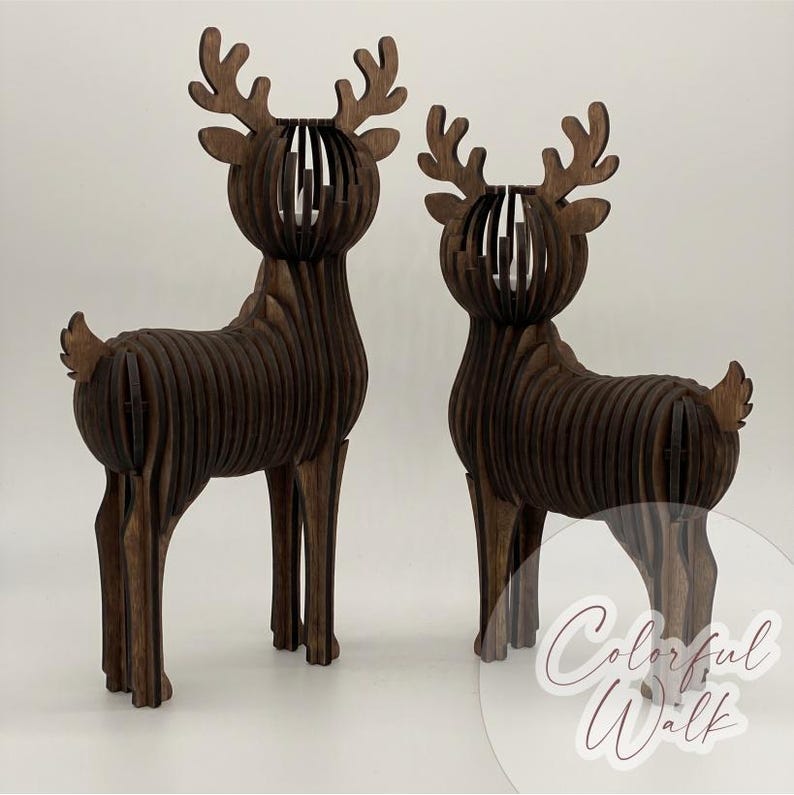 Puede incluir: Dos esculturas de renos de madera marr&oacute;n oscuro. Los renos est&aacute;n construidos con piezas de madera en capas, con secciones abiertas en la cabeza y el cuerpo. Las astas son detalladas. Fondo blanco liso.