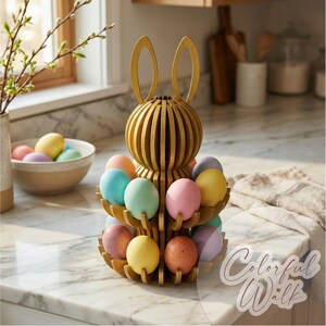Puede incluir: Un soporte para huevos con forma de conejito de Pascua de madera dorada con dos niveles, lleno de huevos de colores pastel. El conejito tiene orejas largas y un cuerpo esf&eacute;rico. Un cuenco con huevos y un jarr&oacute;n con ramas est&aacute;n en el fondo.