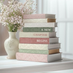 Puede incluir: Una pila de libros con cubiertas estampadas florales en tonos rosa, crema y verde. Las lomos muestran las palabras "A New Chapter Begins". Un jarrón de flores blancas está al lado de los libros. Los libros miden unos 20 cm de alto.