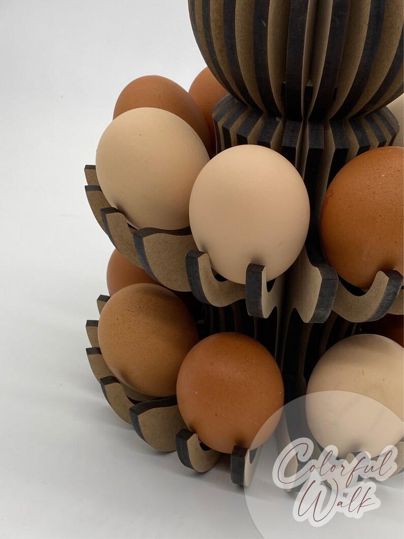Puede incluir: Un portahuevos de madera de varios niveles con un dise&ntilde;o decorativo, lleno de huevos marrones y beige. El soporte tiene una combinaci&oacute;n de colores marr&oacute;n oscuro y beige. Los huevos son de diferentes tonos de marr&oacute;n y beige. El dise&ntilde;o es moderno y funcional.