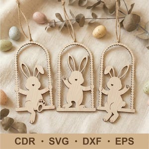 May include: Three wooden Easter bunny ornaments hanging from twine. Each bunny is on a swing inside an arched frame. The bunnies have heart-shaped noses and are surrounded by decorative Easter eggs. The bottom of the image has the text: CDR • SVG • DXF • EPS.