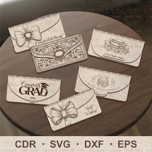 May include: A collection of laser-cut greeting cards with various designs. Some cards feature bows, ornate patterns, or the phrases "Congratulations!", "Best Wishes!", "Congrats Grad 2026", and "A New Chapter Begins". The cards are on a wooden surface.