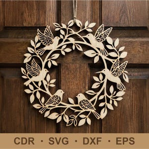 Op de afbeelding: Houten krans met lasergesneden vogels en bladeren. De krans toont verschillende vogels die op takken met bladeren zitten. De krans hangt aan een bruine houten deur. De onderkant van de afbeelding bevat de tekst: CDR • SVG • DXF • EPS.