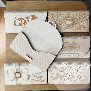 May include: Wooden laser-cut decorative boxes with various designs. One box says "Congrats Grad" with a graduation cap. Another says "Happy Birthday!" and features a bow. Other boxes have floral and ornate patterns.