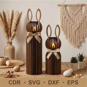 May include: Two wooden bunny-shaped candle holders with a brown finish. Each has a spherical head with vertical slats and a pair of upright ears. A burlap bow adorns the larger bunny, while the smaller one has a lace bow. The base has the text: CDR • SVG • DXF • EPS.