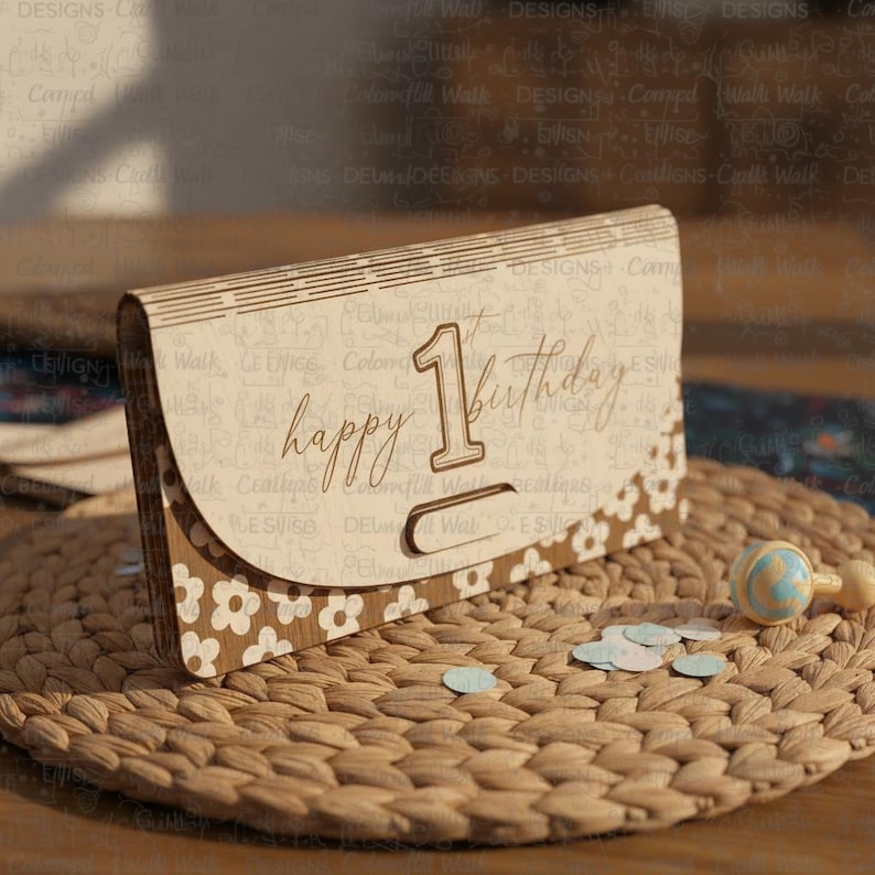May include: A wooden birthday card with the words "happy 1st birthday" engraved on the front. The card has a floral design and is sitting on a woven mat with confetti and a rattle.