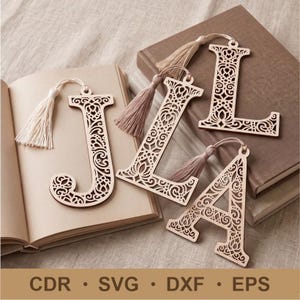 May include: Three light-colored wooden bookmarks shaped like the letters J, L, and A, featuring intricate laser-cut filigree patterns and attached beige fabric tassels. The text CDR, SVG, DXF, EPS is printed at the bottom of the image.