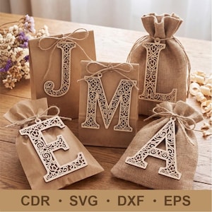 Könnte beinhalten: Vier hellbraune Geschenktüten aus Papier und Jute, jeweils mit einer Jutekordel gebunden und mit einem lasergeschnittenen Holzbuchstaben J, M, L oder E versehen. Die Buchstaben haben filigrane Muster. Text CDR, SVG, DXF, EPS unten.