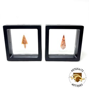 May include: Two small, brown and orange arrowheads are displayed in black shadow boxes. The arrowheads are displayed on a white background.