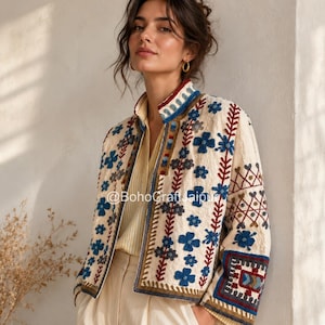 Peut inclure: Une veste blanc cassé ornée de broderies complexes dans des tons de bleu, rouge et marron. Le motif comprend des fleurs, des formes géométriques et un col montant. Le texte @BohoCraftJaipur est visible au centre du vêtement.