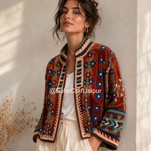May include: A rust-coloured velvet jacket featuring a mandarin collar and intricate floral embroidery in shades of blue, green, and cream. The garment displays the text @BohoCraftJaipur and is worn over a plain white top and light-coloured trousers.