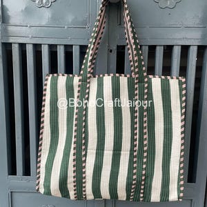 Op de afbeelding: Een rechthoekige tote bag met een verticaal gestreept patroon in donkergroen en gebroken wit. De tas heeft twee schouderbanden en een dunne rood-witte decoratieve bies langs de randen en banden. De tekst @BohoCraftJaipur is zichtbaar.