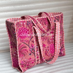 May include: A pink tote bag with a floral pattern in shades of pink and magenta. The bag has matching handles and trim with a striped design. The text "Jaipurcraftstextile" is visible on the bag.