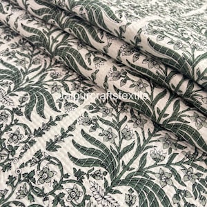 May include: Folded white fabric featuring a repeating pattern of green floral and leaf motifs. The fabric has a quilted texture, with stitching creating a grid pattern. The design combines natural elements with a textile aesthetic, suitable for various home decor items.