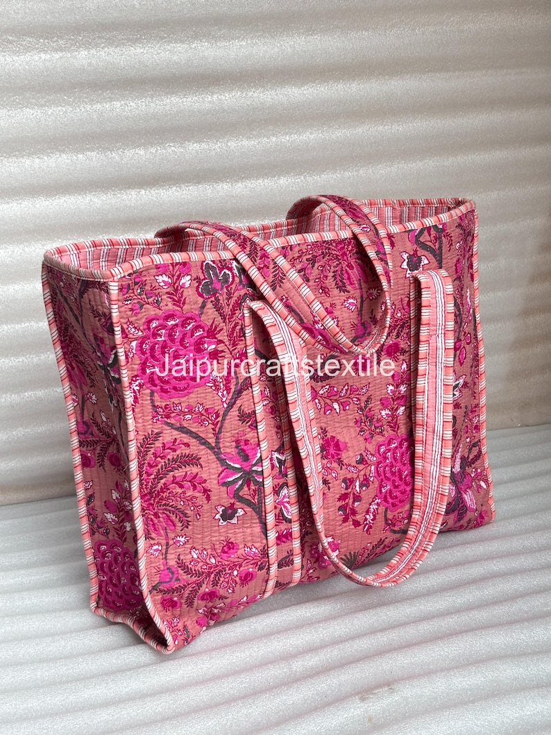May include: A pink tote bag with a floral pattern in shades of pink and magenta. The bag has matching handles and trim with a striped design. The text "Jaipurcraftstextile" is visible on the bag.