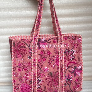May include: A pink tote bag with a floral pattern in shades of pink and magenta. The bag has long handles and a rectangular shape. The text "jaipurcraftstextile" is visible on the bag.
