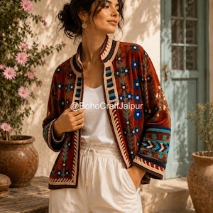 May include: A rust-colored velvet jacket featuring intricate floral embroidery in blue, green, and cream. The garment has a mandarin collar, long sleeves with patterned cuffs, and a front opening with the text BohoCraftJaipur printed on it.