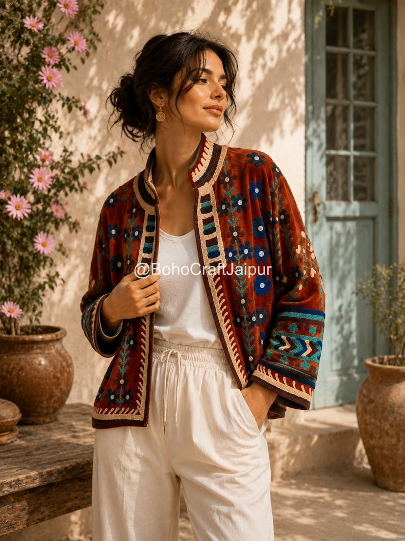 May include: A rust-colored velvet jacket featuring intricate floral embroidery in blue, green, and cream. The garment has a mandarin collar, long sleeves with patterned cuffs, and a front opening with the text BohoCraftJaipur printed on it.
