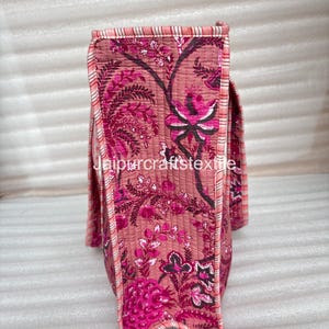 May include: A quilted tote bag with a floral pattern in shades of pink and magenta. The bag features a repeating design of stylized flowers and foliage. The edges are trimmed with a striped fabric in pink and white. The text "jaipurcrafttextile" is visible.
