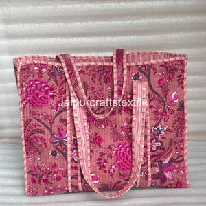 May include: A quilted tote bag with a floral pattern in shades of pink and magenta. The bag has two handles and a rectangular shape. The text "Jamurcraftstextile" is visible on the bag.