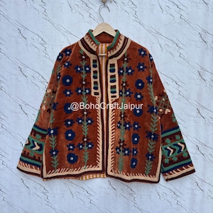 May include: A rust-colored jacket featuring intricate embroidery in dark blue, green, and cream. The design includes floral patterns, geometric borders, and a high collar. The text @BohoCraftJaipur is printed across the center of the garment.