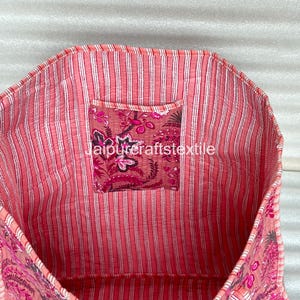 May include: Open view of a pink tote bag with a floral pattern and striped lining. The bag has a small pocket with a floral design and the text "jaipurcraftstextile". The bag is made of a soft, quilted fabric.