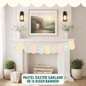 May include: A pastel Easter garland with the text "HE IS RISEN!" hangs above a fireplace. The banner features pastel-coloured pennants with white scalloped edges. The image also includes a framed landscape painting, potted plants, and decorative lighting.