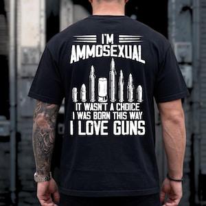 Puede incluir: Camiseta negra con texto blanco e ilustraciones de balas. El texto dice "I'M AMMOSEXUAL, IT WASN'T A CHOICE I WAS BORN THIS WAY I LOVE GUNS". La camiseta tiene cuello redondo y mangas cortas.