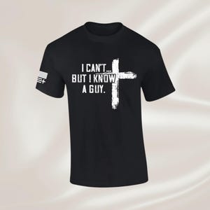 May include: Black t-shirt with the text "I CAN'T... BUT I KNOW A GUY." in white, along with a white cross graphic. The left sleeve features a small American flag design.