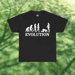 May include: Black t-shirt with a white graphic depicting the evolution of humans, ending with a person kneeling before another. The word "EVOLUTION" is printed in white below the graphic. The shirt has a crew neck and short sleeves.
