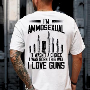 Puede incluir: Camiseta blanca con el texto "I'M AMMOSEXUAL" sobre un gr&aacute;fico de balas y el texto "IT WASN'T A CHOICE I WAS BORN THIS WAY I LOVE GUNS" en negro. La camiseta se est&aacute; usando.