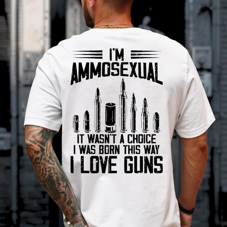 Puede incluir: Camiseta blanca con el texto "I'M AMMOSEXUAL" sobre un gr&aacute;fico de balas y el texto "IT WASN'T A CHOICE I WAS BORN THIS WAY I LOVE GUNS" en negro. La camiseta se est&aacute; usando.