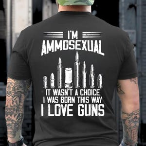 Puede incluir: Camiseta negra con texto blanco e ilustraciones de balas. El texto dice: "I'M AMMOSEXUAL, IT WASN'T A CHOICE I WAS BORN THIS WAY I LOVE GUNS."