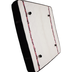May include: A white mattress with two pink and black patterned straps attached to the top and bottom of the mattress. The straps are secured with black metal clips.