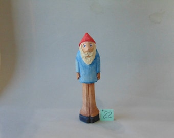 May include: A wooden figurine of a gnome with a red hat, blue shirt, and a white beard. The gnome is standing on a wooden base. The figurine is labeled with the number "22".