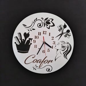 May include: White round clock with black hands and black numbers. The clock has a black and white design with a woman's face, scissors, and hair styling tools. The word "Coafon" is written in brown cursive lettering.