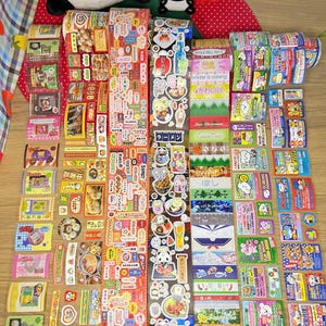 May include: A selection of vibrant decorative stickers, many with Japanese text and illustrations. The stickers showcase diverse designs, including food, animals, and seasonal motifs. Some stickers feature text that reads "Winter is coming" and "Angle Bell Rock".