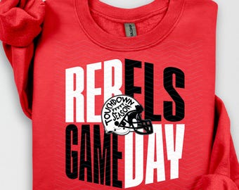 May include: A red sweatshirt with the words "REBELS GAME DAY" in white and black block letters. A football helmet graphic is centered between the words. The words "TOUCHDOWN SEASON" are on the helmet.