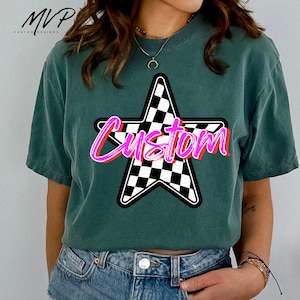 May include: Dark teal t-shirt with a star design featuring a black and white chequered pattern. The word "Custom" is written across the star in a pink and red font. The shirt has short sleeves and a crew neck.