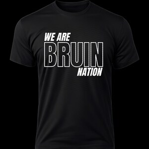 Può includere: T-shirt nero con la scritta bianca "WE ARE BRUIN NATION". Il testo è in grassetto, con contorno. La maglietta ha un girocollo e maniche corte. Lo sfondo è nero.