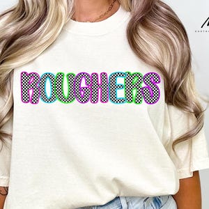 May include: Cream-colored t-shirt with the word "ROUGHERS" in a colorful, checkered design. The letters are outlined in blue, green, and purple, with a black and white checkered pattern filling each letter. The shirt has short sleeves.