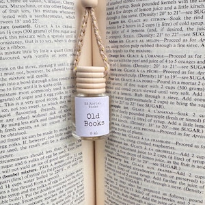 May include: A small glass bottle with a wooden cap hangs from a gold-colored cord. The bottle has a label that reads "Old Books" and "8 ml" against a backdrop of aged book pages.