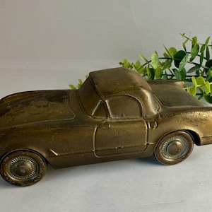 May include: A vintage brass car figurine with a classic convertible design. The car has detailed wheels and a weathered finish, suggesting age. The overall color is a warm, antique gold. The car is a decorative item.