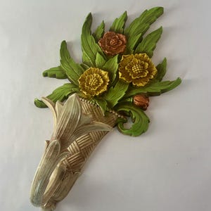 May include: A decorative wall sconce featuring a bouquet of flowers. The flowers are yellow and orange, with green leaves. The sconce is a light beige color with a woven basket design.