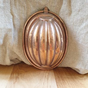 May include: A vintage copper mold for baking a fluted cake or dessert. The mold has a rounded shape with a handle on top.