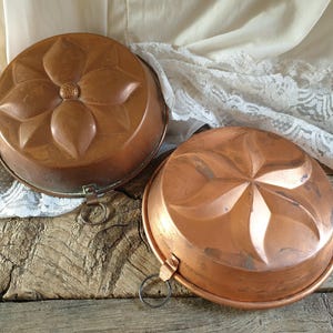 May include: Two antique copper cake molds with floral designs. The molds have a shiny copper finish and are in good condition.