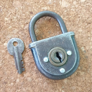 May include: A vintage padlock with a key. The padlock is made of metal and has a black finish. The key is made of metal and has a silver finish.